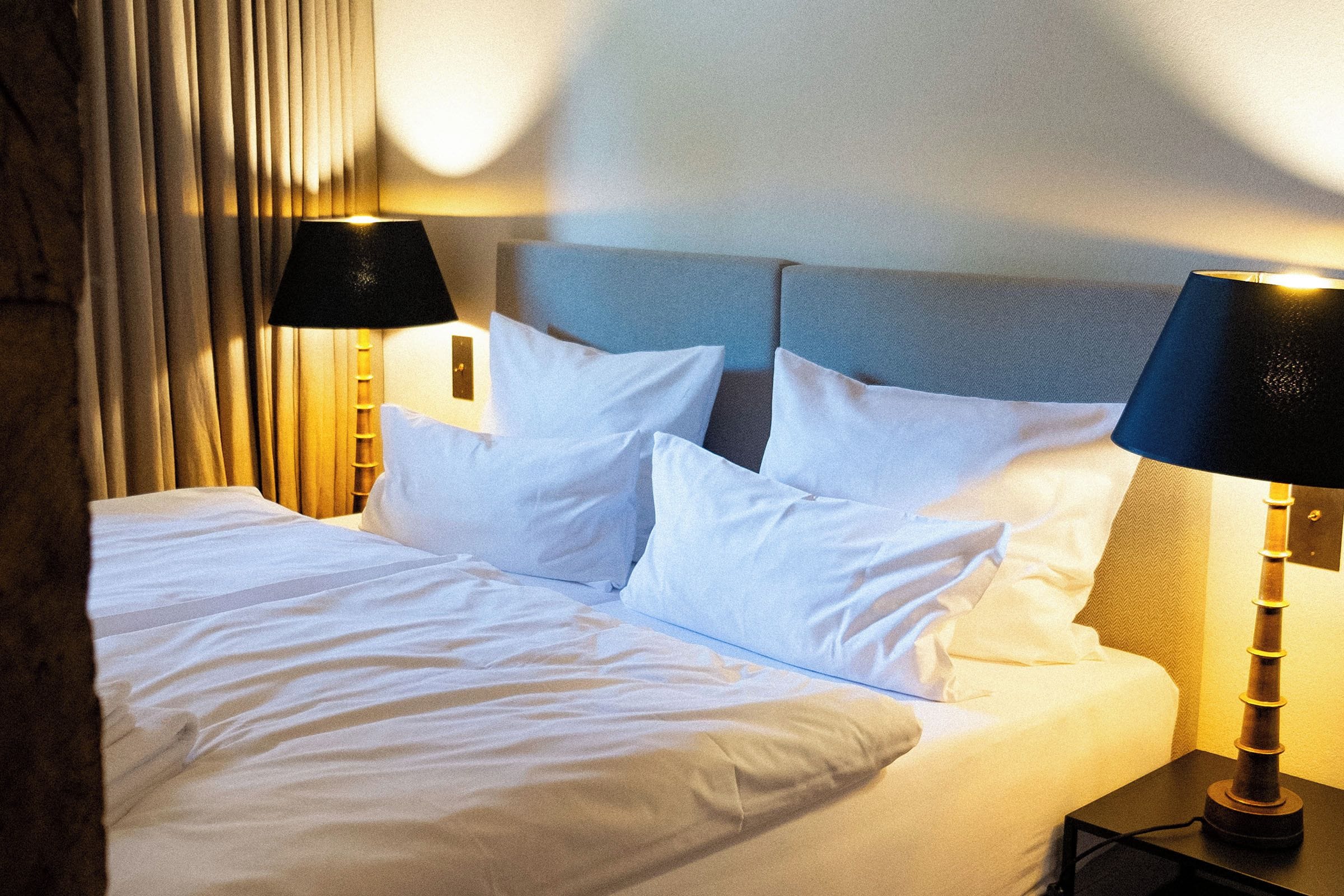 Una cama bien hecha con sábanas y almohadas blancas, con dos lámparas de noche con abat-jour negros a cada lado.
