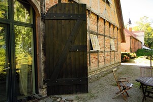 Un edificio rústico con una puerta de madera grande, un muro de ladrillo y un patio de grava con una silla y una mesa.