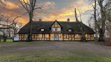 Ein traditionelles Fachwerkhäuschen mit einem Reetdach, mehreren Fenstern und einem gepflegten Rasen.