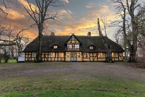 A traditional half-timbered house with a thatched roof, multiple windows, and a well-maintained lawn. - Gut Damp (Damp)