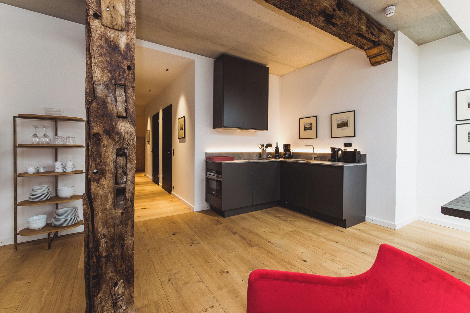 Une cuisine moderne avec des meubles de couleur sombre, un plancher en bois et une chaise rouge au premier plan.