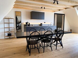 Zona pranzo con un tavolo lungo e sedie, una cucina sullo sfondo e un soffitto in legno.