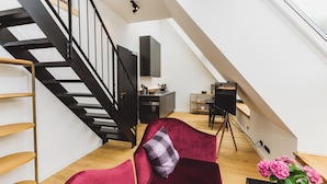 A modern loft with a black staircase, a red velvet sofa, a dining area, and a kitchen. - Gut Damp (Damp)