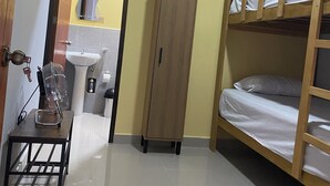 A compact room with a bunk bed, a wooden wardrobe, a small table with a fan, and a bathroom visible through an open door. - Hotel Royal Mancora (Máncora)