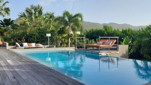A poolside area with lounge chairs, a wooden deck, and lush greenery. - Jardin d'O résidence naturiste couples only (Orient Bay)