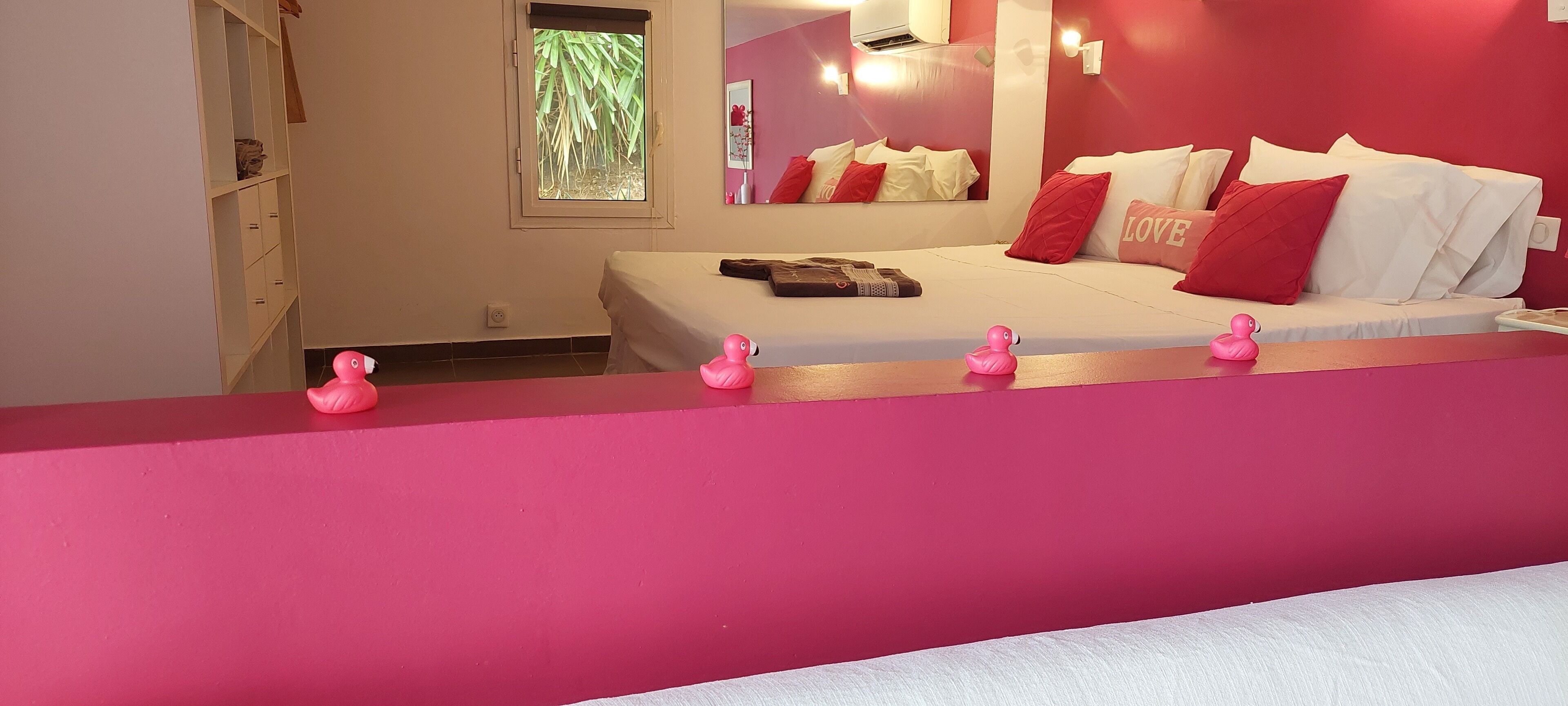 Une chambre à coucher avec un lit, des oreillers, une table de chevet et un canard en plastique rose.