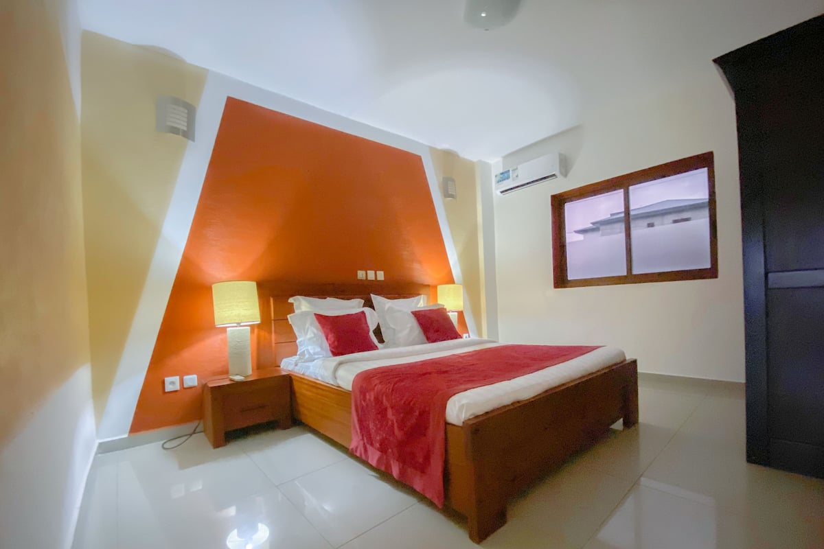 A bedroom with a bed, nightstands, a red throw blanket, and a window with a view.