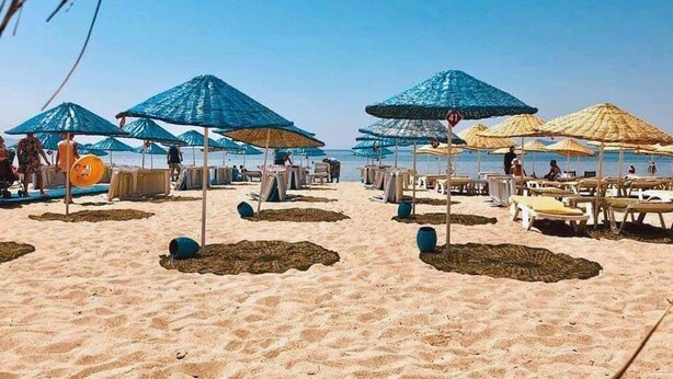 A beach with rows of umbrellas and sun loungers, some with people under them. - Milestone Otel (Ayvalik)