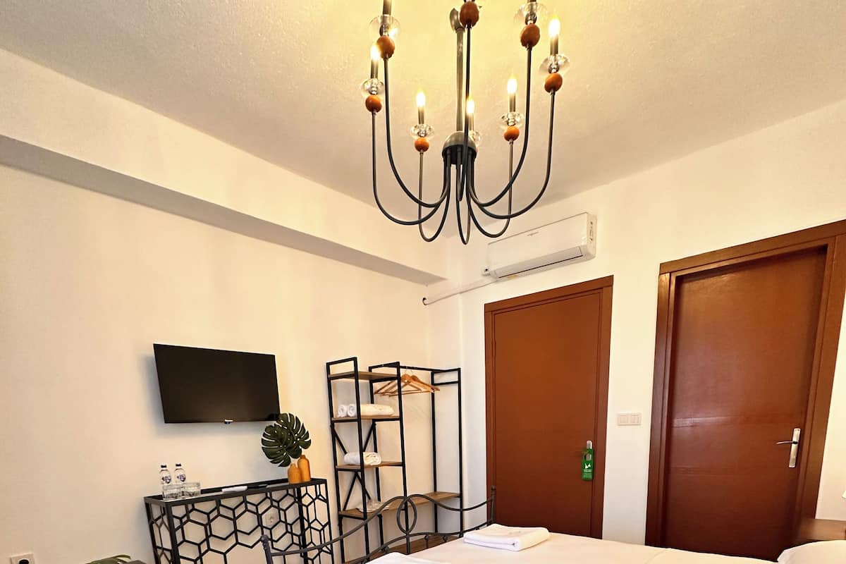 Une chambre d’hôtel avec un lit, une télévision, un bureau agrémenté d’une plante, une armoire et un lustre.