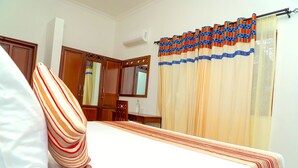 Une chambre d’hôtel avec un lit, une armoire en bois, un miroir et une fenêtre avec des rideaux.