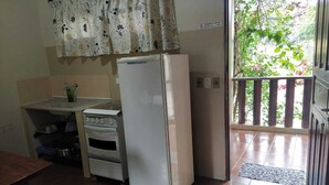 Une cuisine équipée d’un réfrigérateur, d’un four et d’une fenêtre donnant sur un espace verdoyant.