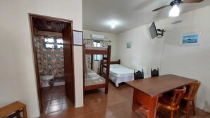 Une chambre de dortoir avec un lit superposé, une petite table et des chaises. On y trouve un ventilateur de plafond, un appareil de climatisation et une fenêtre avec des rideaux.