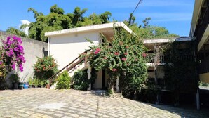 Une cour intérieure avec un escalier menant à un bâtiment, le tout entouré de plantes en pot et d’arbres en fleurs.