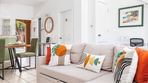 A modern living room with a beige sofa, green and orange patterned cushions, a dining area with a wooden table and chairs, and a framed picture on the wall. - Family-Friendly Oasis near Disney and Theme Parks (Kissimmee)