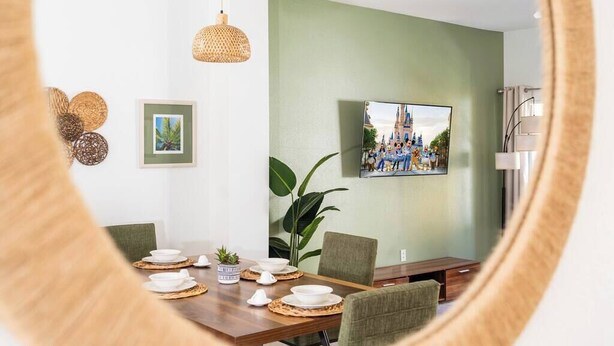 A dining area with a wooden table set for four, a large green wall, and a framed picture above the table. - Family-Friendly Oasis near Disney and Theme Parks (Kissimmee)