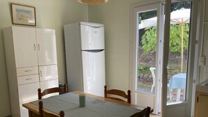 A dining area with a table and chairs, a refrigerator, a cabinet, and a door leading to an outdoor area with a table and chairs. - Maison Centre Ville de Soulac, 5 mn à Pied du Centre et de la Plage (Soulac-sur-Mer)