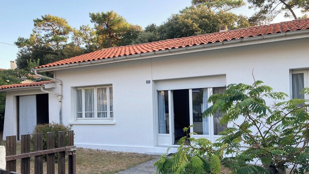 A white building with a red-tiled roof, a wooden fence, and a tree in the foreground. - Maison Centre Ville de Soulac, 5 mn à Pied du Centre et de la Plage (Soulac-sur-Mer)