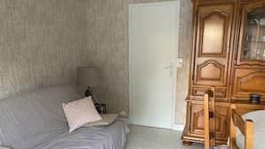 A room with a grey sofa, patterned pillows, a wooden cabinet, and a chair. - Maison Centre Ville de Soulac, 5 mn à Pied du Centre et de la Plage (Soulac-sur-Mer)