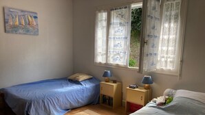 A bedroom with two beds, a window with lace curtains, a painting on the wall, and a wooden floor. - Maison Centre Ville de Soulac, 5 mn à Pied du Centre et de la Plage (Soulac-sur-Mer)