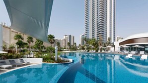 A modern hotel with a large swimming pool, palm trees, and high-rise buildings in the background. - Maison Privee - Tranquil Apt w/ Mesmerizing Views cls to Marina (Dubai)