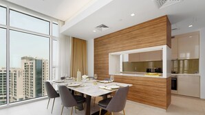 A modern dining area with a large window, a wooden accent wall, and a kitchen visible through an open door. - Maison Privee - Tranquil Apt w/ Mesmerizing Views cls to Marina (Dubai)