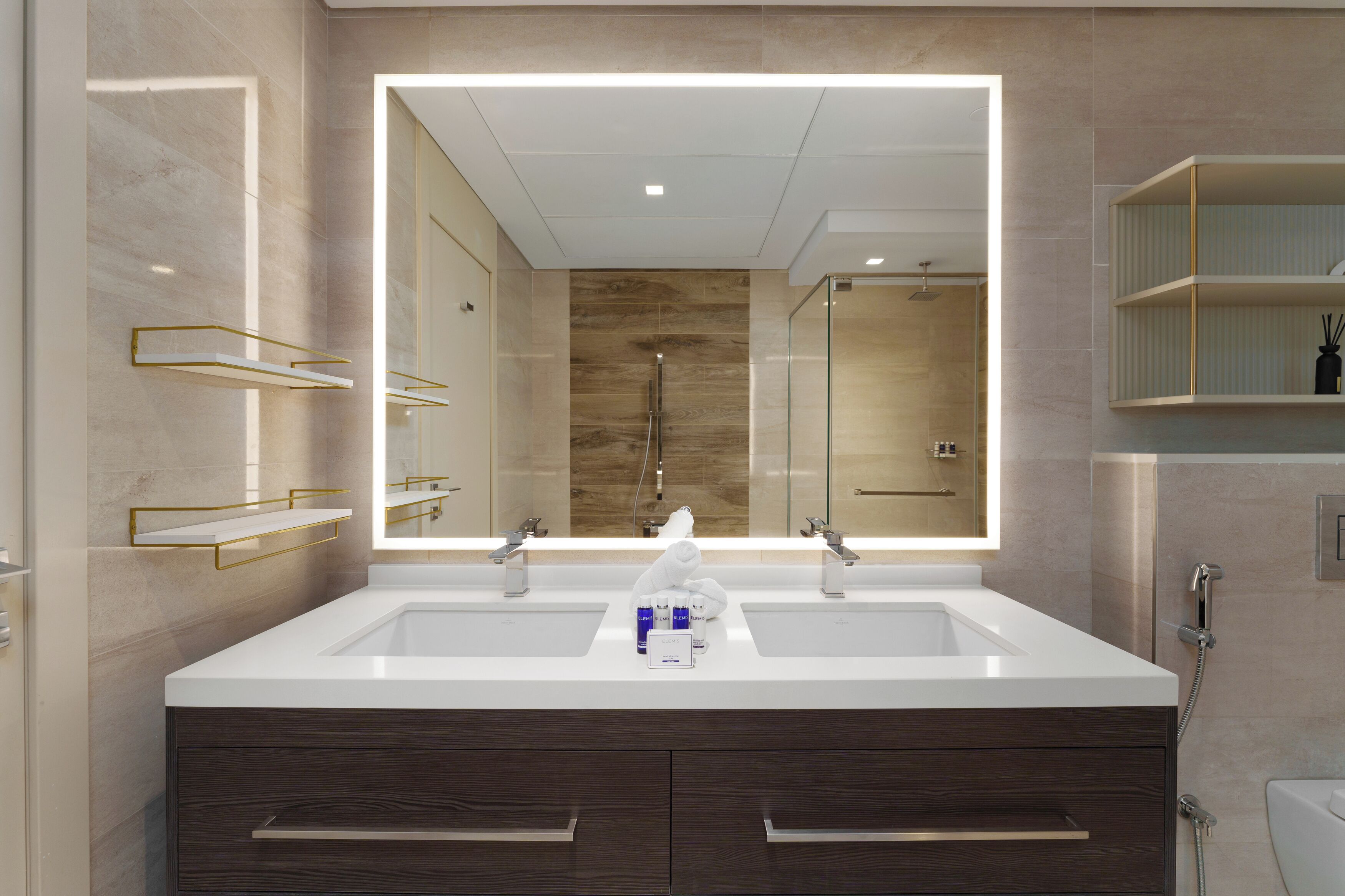 A modern bathroom with a large mirror, two sinks, and a shower.