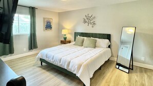A bedroom with a bed, a standing mirror, a nightstand, a lamp, and a window with curtains. - Charming large 2-bedroom house 15 min to beach (Palm Coast)