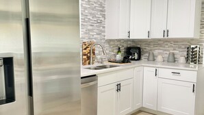 A modern kitchen with white cabinets, a stainless steel refrigerator, and a tiled backsplash. - Charming large 2-bedroom house 15 min to beach (Palm Coast)