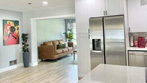 A modern kitchen with white cabinets, a stainless steel refrigerator, and a hanging pendant light. - Charming large 2-bedroom house 15 min to beach (Palm Coast)