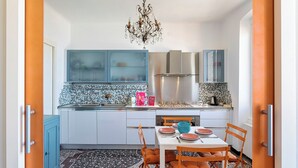 A compact kitchen with blue cabinets, a tiled backsplash, and a dining area with orange chairs and a white table. - Camogli Gulf View by Wonderful Italy (Camogli)