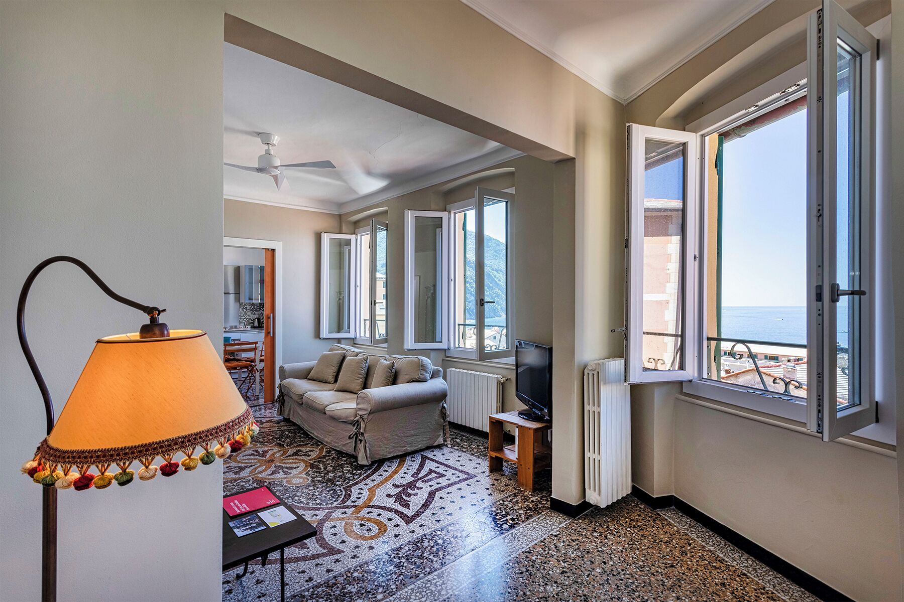 Habitació d'hotel amb sofà, televisió, làmpada i finestres grans que donen vistes al mar.