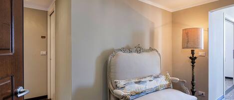 Un couloir avec une porte en bois, un fauteuil blanc recouvert de tissu avec un coussin décoratif et un lampadaire.