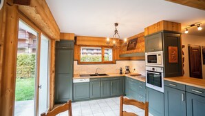 A kitchen with wooden cabinets, a sink, a stove, and a dining area with chairs. - Chalet 9 persons, near Linga gondola, with Wi-Fi - Chatel Reservation (Châtel)