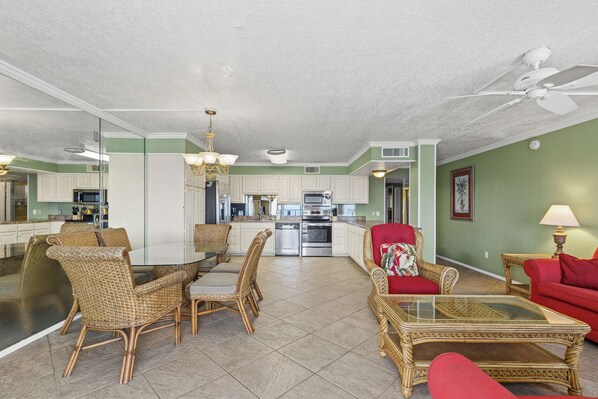 A spacious living area with a dining table, wicker chairs, a red armchair, and a glass coffee table.