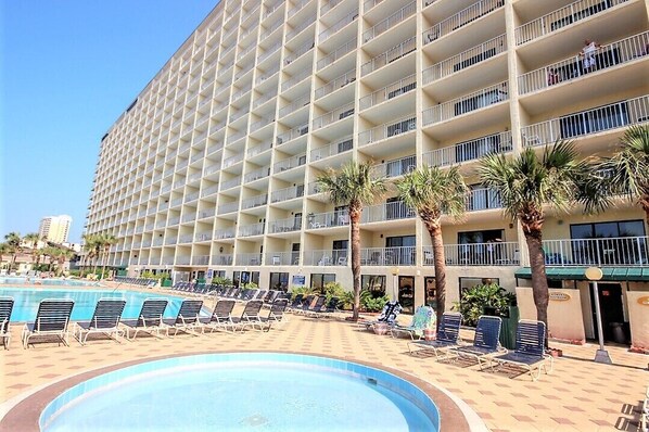 Ett stort hotell med flera balkonger, en swimmingpool och palmer.