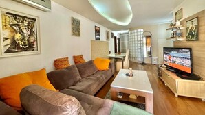 A modern living room with a sofa, coffee table, TV, and artwork on the walls. - Family Two Bedroom Apartment Vasko (Budva)