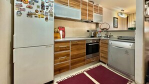 A compact kitchen with wooden cabinets, a refrigerator, an oven, a dishwasher, and a coffee maker. - Family Two Bedroom Apartment Vasko (Budva)