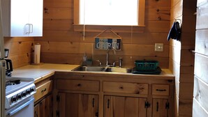 Una cocina compacta con armarios de madera, un lavamanos, una estufa y una ventana con persianas.