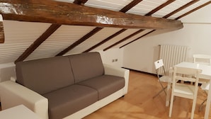 A room with a brown sofa, white table, and chairs, wooden beams on the ceiling, and a radiator. - Casa Marzia: cosy, quiet, close to the centre and Sant'Orsola Malpighi Hospitals (Bologna)
