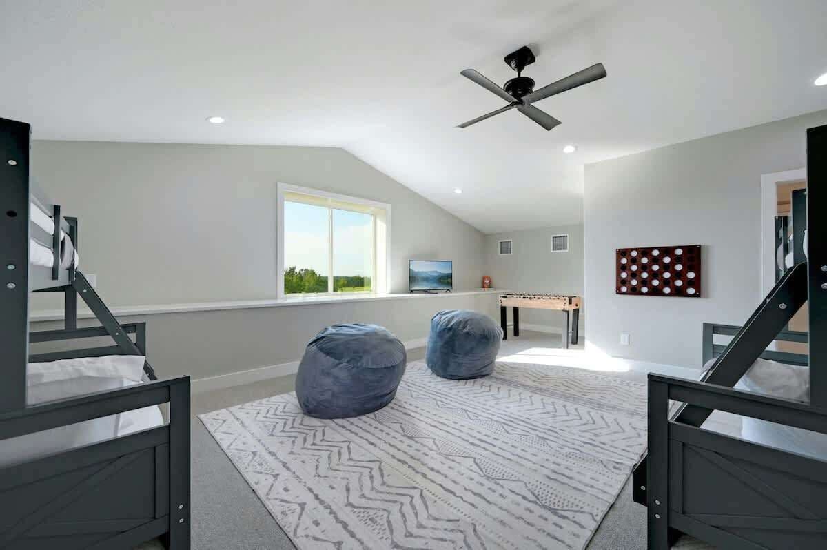 Une pièce comprenant un lit, deux fauteuils en forme de poire, un ventilateur de plafond, une fenêtre et un tableau au mur.