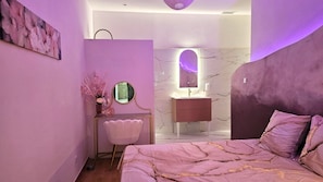 A modern bedroom with a bed, a vanity with a mirror, and a wall-mounted artwork.
