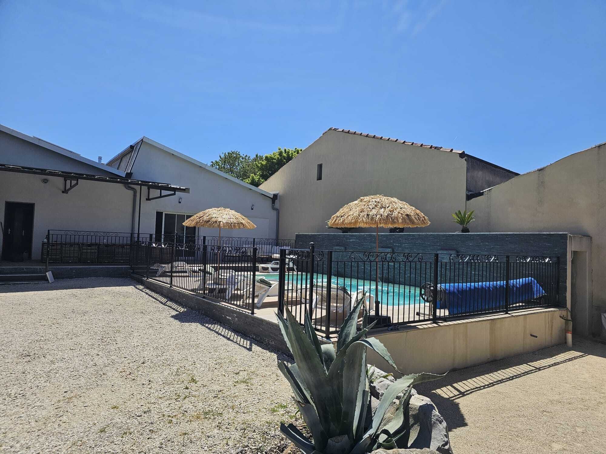 A swimming pool area with two umbrellas, a fenced pool, and a building with a white exterior.