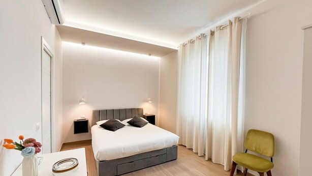 Une chambre moderne comprenant un lit, des tables de chevet, un bureau, une chaise et une fenêtre avec des rideaux.