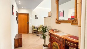 Un couloir avec une porte en bois, un coin repas avec des chaises, une plante en pot, une table en marbre et une bibliothèque remplie de livres.