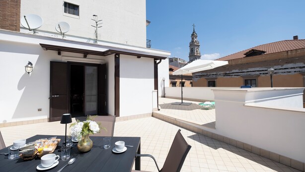 Een terras op het dak, met een eettafel, schotels en een klokkentoren op de achtergrond.