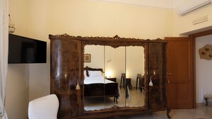 Een slaapkamer met een groot spiegelkastje, een witte fauteuil, een bed en een aan de muur bevestigde televisie.