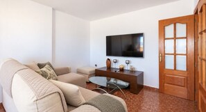 A living room with a beige sofa, a glass coffee table, a flat-screen TV mounted on the wall, and a wooden door with glass panels. - La Noria Floor 1 (Torre Del Mar)
