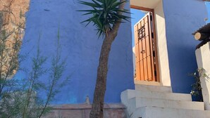Un edificio con un muro azulado, una palmera y una verja.
