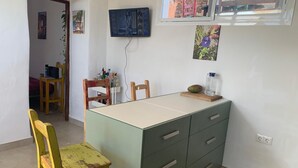 Una cocina pequeña con una mesa de comedor, sillas, un televisor montado en la pared y un ventanal con vistas al exterior.