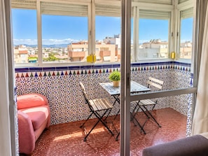 Un balcon avec vue sur le paysage urbain, un canapé rouge, une petite table avec une plante et une chaise pliante.